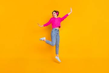 Full size photo of pretty funky lady jump high have fun listen earphones wear pullover isolated yellow color background