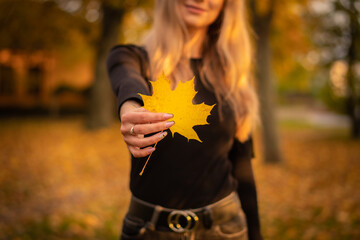 Portrait of a young smiling woman in the park on the blurred background. She is holding fallen leaves in his hand.