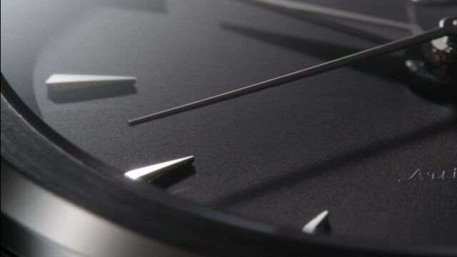 Extreme closeup of metallic second arrow passing by on black clock face. Lengthwise view of luxury swiss watch 