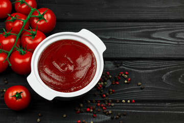 ketchup in a plate with red tomatoes, round peppers and bay leaves on a black wooden background. Making ketchup