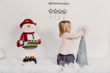 Little girl at christmas scene playing with a snowman doll.