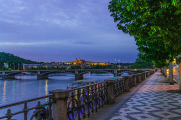 Obraz premium Prague with promenade riverside road, Prague Castle, St. Vitus Cathedral in Hradcany district, bridges over Vltava river, night evening twilight view, Bohemia, Czech Republic