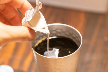 タンブラーに入ったコーヒーにミルクを入れる