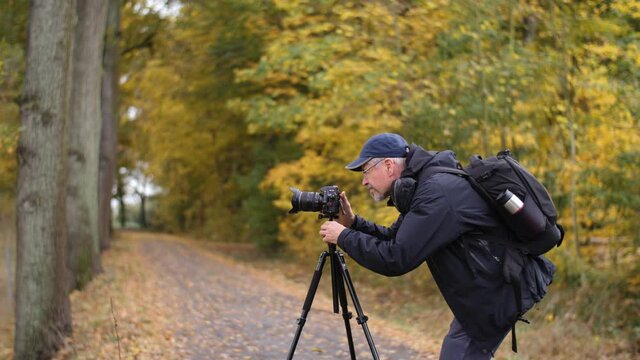 Mature photographer taking pictures in nature in late autumn with a DSLR camera. Male Caucasian travels outdoors with a professional camera. Beautiful forest background. Using a tripod, camera stand.