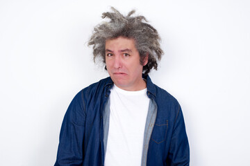 Fototapeta na wymiar Handsome middle aged Caucasian man with afro gray hair, against white wall, being nervous and scared biting lips looking camera with impatient expression, pensive.