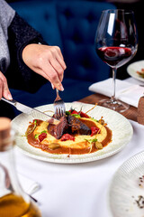 Female hands cut meat in a plate.