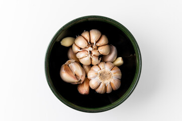 A lot of Garlic cloves and pieces of raw garlic in bowl on isolated white background. Top view Garlic bulbs with blank space.