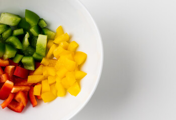 Raw mixed red yellow and green bell pepper cut into small pieces put on a bowl. Healthy vegetables and food on isolated white background.