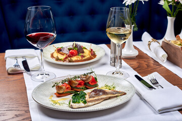 A fish dish and a meat dish and two glasses of wine.