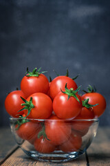 Fresh cherry tomatoes in a glass bowl on a wooden background