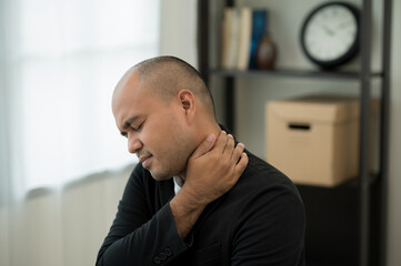 Naklejka premium Business Asian man in suit sitting in home working with laptop he has shoulder neck pain and hurt get stress a symptom office syndrome.