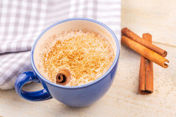Blue cup of salep milky hot drink of Turkey with cinnamon powder and sticks healthy spice and autumn winter içeceği on white rustic vintage wooden table.
