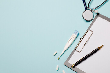 Pharmaceuticals, electronic thermometer, pills, stethoscope, notepad and pen on a blue background. Copy space