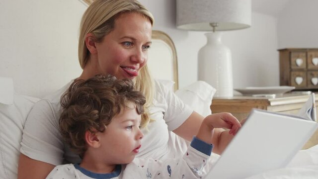 Mother looking at picture book with son wearing pyjamas before going to sleep - shot in slow motion