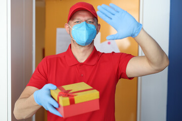 Fototapeta na wymiar Courier in protective medical mask and gloves holds gift box in his hands. Safe delivery of parcels in the coronavirus pandemic concept