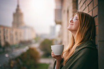 Beautiful young woman enjoying morning coffee on the balcony of house city view center in the...