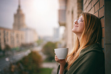 Beautiful young woman enjoying morning coffee on the balcony of house city view center in the sunlight, Moscow