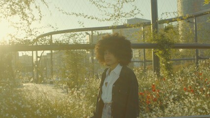 Portrait of mixed race black woman in the park full of flowers. Laughing in contour sunlight and watching the camera. Cinema film colors