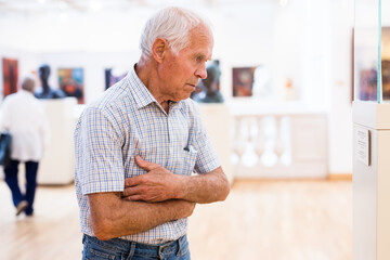 mature European man examines paintings in an exhibition in hall of an art museum