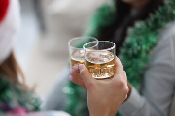 They are holding two glasses with liquid in their hands against background of New Year's garlands. Celebrating Christmas and New Years concept