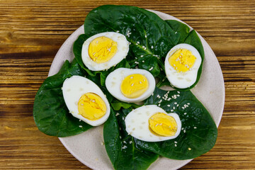 Boiled eggs with fresh spinach leaves and sesame seeds on wooden table. Top view