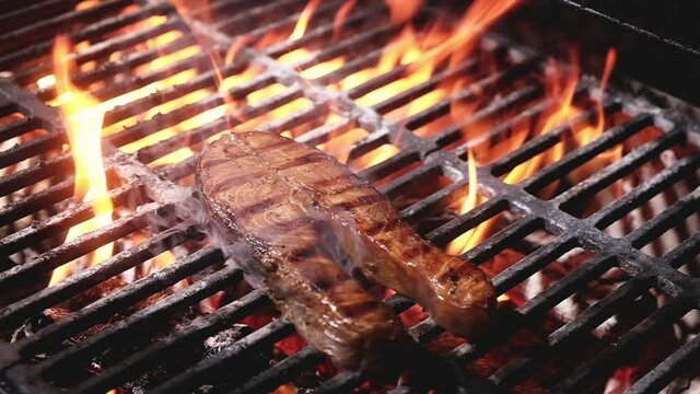 Juicy salmon steak with strips is grilled on a barbecue in a flame of fire and smoke. Seafood on the grill. cooking seafood on charcoal grill at picnic and bbq. Preparing food at the camp outside