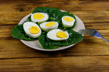 Boiled eggs with fresh spinach leaves and sesame seeds on wooden table