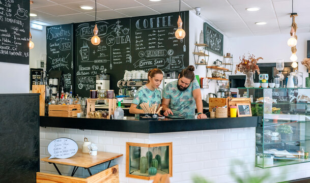 Owners of a coffee shop working looking at the tablet leaning on the counter