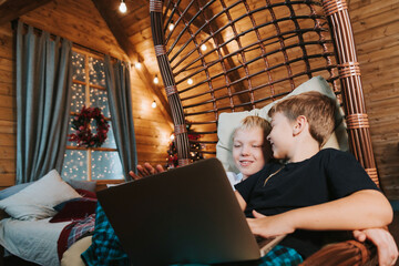 Obraz na płótnie Canvas children two boys sit in a hammock in a Christmas interior and having a video chat by laptop