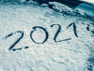 The numbers of the New Year 2021 are written on the snow-covered glass of the car. Travel route concept in winter season.