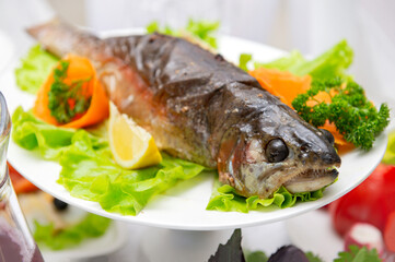 cooked baked trout with lemon on a lettuce leaf on a white platter