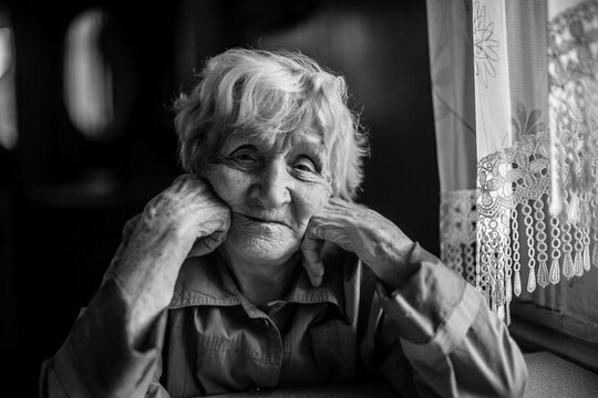 An elderly woman in the house sitting at the table. Black and white photography.