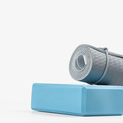 Rolled blue yoga mat and light blue foam block or brick. Gender neutral fitness and exercise concept accessories with copy space. Active lifestyle. Workout at home or gym