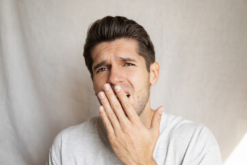 Portrait of a young handsome man with a bored face expression covering his mouth with a hand from yawning 