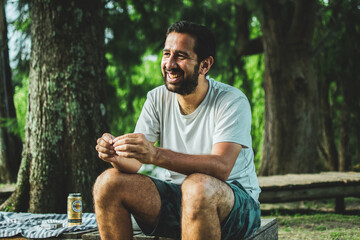 man in white shirt and beard smiling sitting on wooden pier with forest in background on summer vacation