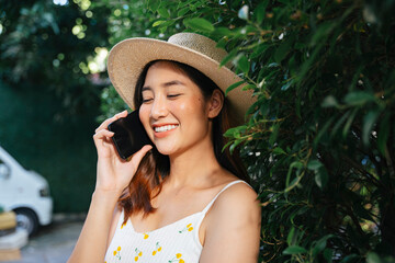 Asian traveler woman wear hat and white dress talking on the phone at park.