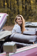 young smiling woman looking at camera while sitting in cabriolet, blurred foreground