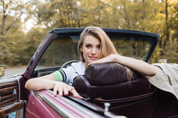 young woman looking at camera while sitting in vintage cabriolet, blurred foreground