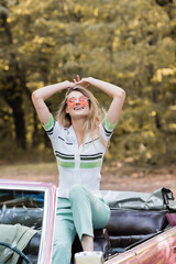 excited young woman relaxing while sitting in cabriolet with raised hands and closed eyes