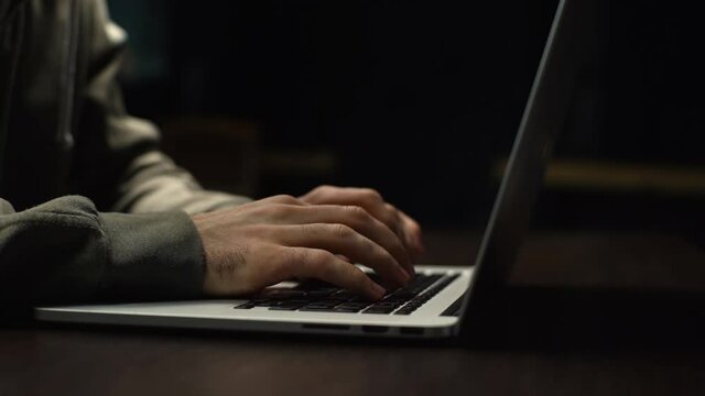 Close-up of unrecognizable hacker man stretching hands and starting to typing on laptop computer keyboard and breaking password. Freelancer using laptop working from home. Tracking shot in slow motion