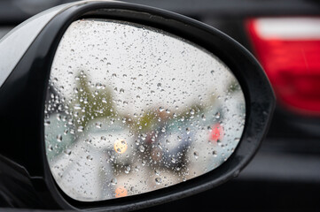 Raindrops on the rear view mirror of a car with the defocused reflection of the cars behind