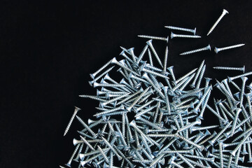 Construction fasteners. Self-tapping screws are scattered in a disorderly heap on a dark background. Excellent design for advertising construction fasteners.