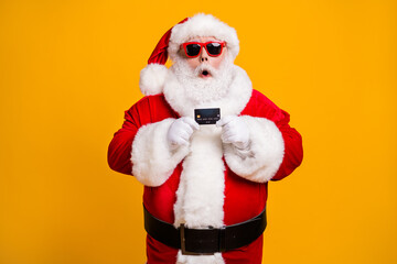 Fototapeta na wymiar Portrait of his he nice attractive amazed stunned wondered Santa holding in hand bank card budget safe shopping investment isolated bright vivid shine vibrant yellow color background