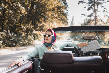 Elegant woman with map sitting on driver seat of roofless auto on blurred foreground
