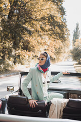 Fototapeta premium Stylish woman in headscarf looking away on driver seat of roofless car