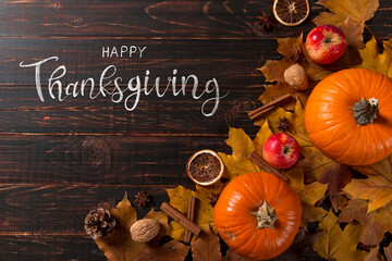 Thanksgiving greetings. Dry yellow leaves, pumpkins, berries, nuts and frame on a wooden background, top view. Kaligraphic capital inscription.