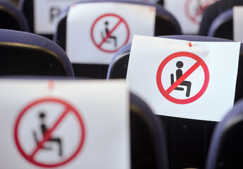 Shallow depth of field with social distance warning signs on seats during a show, concert or play in a theater or cinema, conference hall. Empty rows of places marked with a warning 'don't sit' sign.