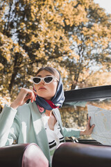 Elegant woman holding map on driver seat of vintage car on blurred foreground