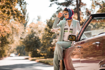 Young woman in sunglasses sitting on car on road on blurred foreground