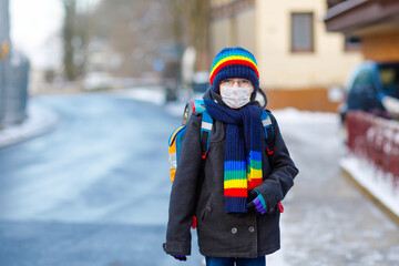 Little kid boy with glasses wearing medical mask on the way to school. Child backpack satchel. Schoolkid on winter day with warm clothes. Lockdown and quarantine time during corona pandemic disease